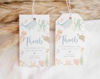 May include: Two light blue and white thank you tags with an ocean theme. The tags feature a whale, octopus, turtle, jellyfish, and coral. The text on the tags reads "Thanks for showering our baby with love!" and "Camilla's Baby Shower".