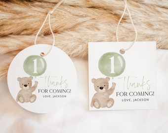May include: Two round thank you tags featuring a brown teddy bear holding a green balloon with the number 1 on it. The text on the tags reads "Thanks for coming! Love, Jackson".