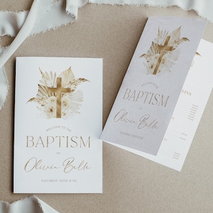 May include: A white card with gold lettering announcing a baptism for Olivia Belle on Saturday, June 30th. The card features a gold cross surrounded by white flowers and dried grasses.