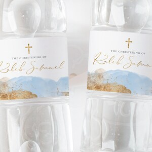 May include: Two clear water bottles with labels that say "The Christening of Kaleb Samuel" in gold lettering. The labels have a blue and gold watercolor background with a gold cross at the top.