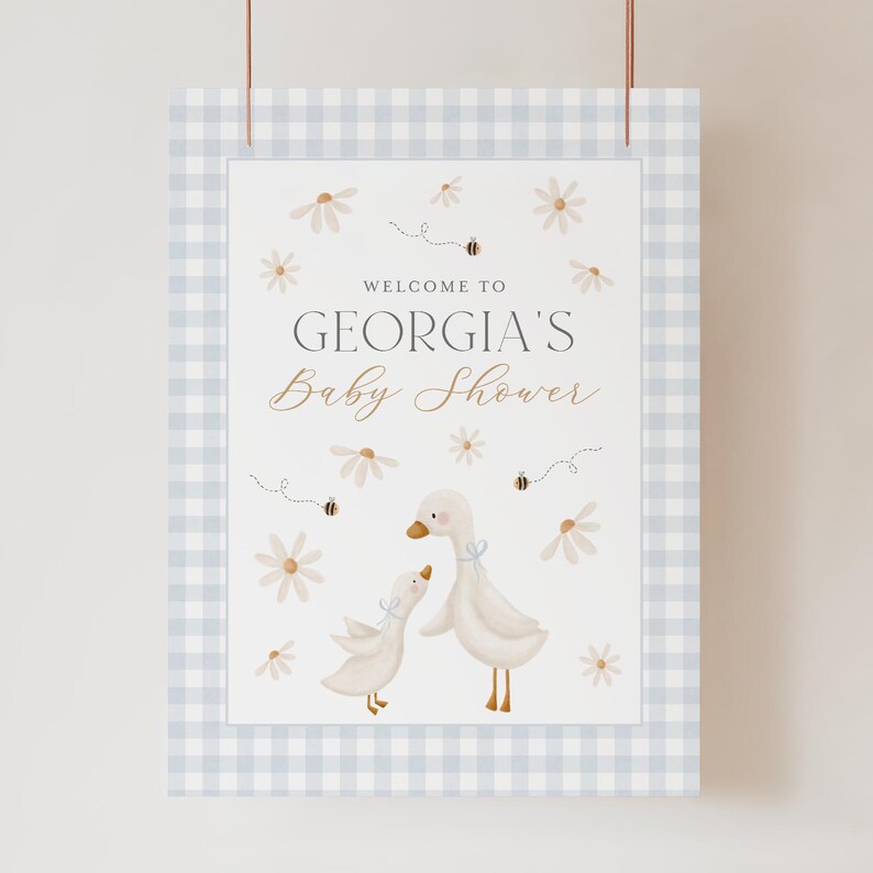 K&ouml;nnte beinhalten: Ein blaues und wei&szlig;es Gingham-Willkommensschild mit dem Text "Willkommen zu Georgias Baby Shower" und einer Aquarell-Illustration von zwei wei&szlig;en G&auml;nsen mit braunen Augen und Schn&auml;beln. Die G&auml;nse sind von wei&szlig;en G&auml;nsebl&uuml;mchen und kleinen braunen Bienen umgeben.