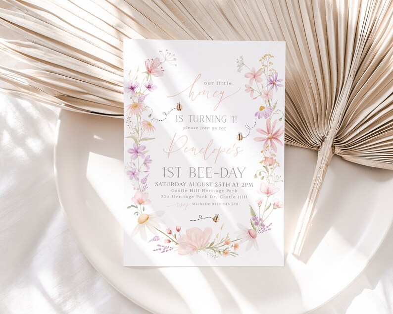 K&ouml;nnte beinhalten: Eine Einladung im floralen Design f&uuml;r eine erste Geburtstagsfeier. Die Einladung zeigt einen Kranz aus Aquarellblumen, Bienen und den Text "our little honey is turning 1! please join us for Penelope's 1st bee-day. Saturday August 25th at 2pm. Castle Hill Heritage Park. 223 Heritage Park Dr. Castle Hill. Michelle 0412 345 678"