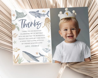 May include: A thank you card with a watercolor illustration of ocean animals, including a whale, shark, and jellyfish. The card has a photo of a baby boy wearing a crown with the number "1" on it. The text on the card reads "Thanks" and "Thank you so much for celebrating my 1st birthday with me and for the wonderful present you gave me! I had such a good time playing with all my friends & eating cake! Love, Charlie."