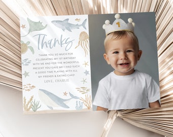 May include: A thank you card with a watercolor illustration of sea creatures, including a whale, a shark, and a jellyfish. The card has a photo of a baby boy wearing a crown with the number 1 on it. The text on the card reads "Thanks" and "Thank you so much for celebrating my 1st birthday with me and for the wonderful present you gave me! I had such a good time playing with all my friends & eating cake! Love, Charlie."