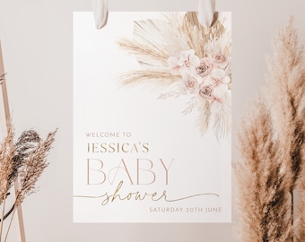 May include: A white sign with gold lettering that says "Welcome to Jessica's Baby Shower" with a date of Saturday 20th June. The sign is decorated with a watercolor illustration of pampas grass and pink roses.