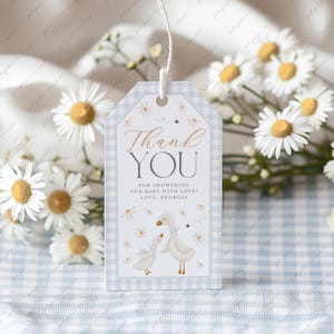 Könnte beinhalten: Blau-weißes Gingham-Dankeschön-Etikett mit weißem Hintergrund, auf dem zwei Comic-Gänse und ein Blumenmuster abgebildet sind. Der Text lautet "Danke" in goldener Schrift und "Für das Duschen unseres Babys mit Liebe! Liebe, Georgia".