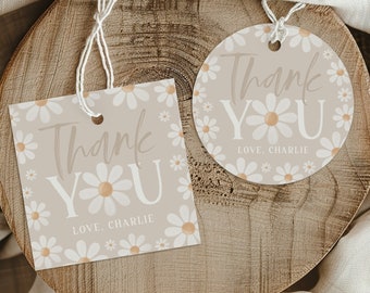 Op de afbeelding: Twee bedank-cadeautjes met een madeliefjespatroon. De kaartjes zijn beige met witte madeliefjes en gouden centra. De tekst op de kaartjes luidt "Bedankt" in een cursief lettertype met "Lieve, Charlie" eronder. Eén kaartje is vierkant en het andere is rond.