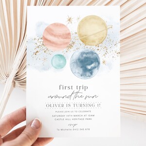 Op de afbeelding: Een aquarel-illustratie van planeten in een galaxie met gouden glitter. De tekst luidt "first trip around the sun OLIVER IS TURNING 1! PLEASE JOIN US TO CELEBRATE SATURDAY 14TH MARCH AT 10AM CASTLE HILL HERITAGE PARK sup To Michelle 0412 345 678"