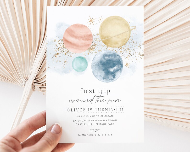 Op de afbeelding: Een aquarel-illustratie van planeten in een galaxie met gouden glitter. De tekst luidt "first trip around the sun OLIVER IS TURNING 1! PLEASE JOIN US TO CELEBRATE SATURDAY 14TH MARCH AT 10AM CASTLE HILL HERITAGE PARK sup To Michelle 0412 345 678"