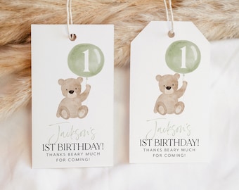 May include: Two green and white favor tags with a brown teddy bear holding a green balloon with the number 1 on it. The text on the tags reads "Jackson's 1st Birthday! Thanks Beary Much for Coming!"