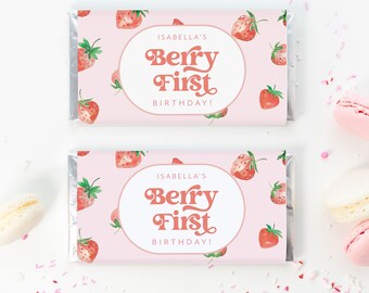 May include: Two pink and white chocolate bar wrappers with a strawberry pattern. The wrappers have a white oval with the text "Isabella's Berry First Birthday!" in a retro font.