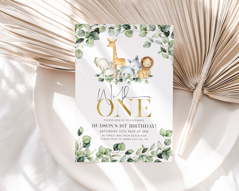 May include: A white invitation with a gold border and green leaves. The text reads "Wild One" in gold letters. The invitation is for Hudson's 1st birthday party. The party is on Saturday, May 15th at 1 PM. The address is 82 Forest Way, Palm Beach NSW. The RSVP number is 0412 345 678.
