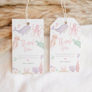 Puede incluir: Dos etiquetas de agradecimiento de color rosa y azul con un diseño de ballena, pulpo, tortuga y medusa. El texto en las etiquetas dice "Gracias" y "Por celebrar mi cumpleaños conmigo!" con un corazón rosa y "Con cariño, Camilla".