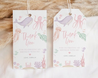 Può includere: Due tag di ringraziamento rosa e blu con un design di balena, polpo, tartaruga e medusa. Il testo sui tag recita "Grazie" e "Per aver festeggiato il mio compleanno con me!" con un cuore rosa e "Con affetto, Camilla".
