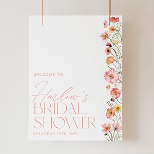 Pu&ograve; includere: Un cartello bianco con accenti floreali rosa e il testo "Benvenuti al Bridal Shower di Harlow Sabato 15 maggio".
