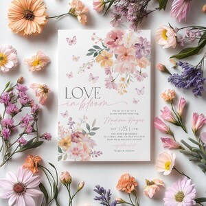 Op de afbeelding: Een bloemige bruidsdouche-uitnodiging met de tekst "LOVE in bloom" en de naam "Madison Hayes". De uitnodiging is versierd met roze, gele en paarse bloemen en vlinders.