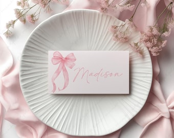 May include: A pink and white place card with a pink bow and the name Madison written in pink cursive.