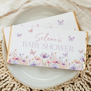 Könnte beinhalten: Ein weißer Schokoladenriegel-Wrapper mit einem Blumendesign und Schmetterlingen. Der Text auf dem Wrapper lautet "Selena's Baby Shower".