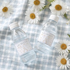 Könnte beinhalten: Zwei durchsichtige Plastikwasserflaschen mit weißen Etiketten. Die Etiketten haben ein florales Design mit goldenen Akzenten und den Text "Georgia's Baby Shower Thanks for coming!"
