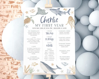 May include: A blue and white illustrated poster with a whale, starfish, and seashells. The poster is titled "Charlie My First Year" and includes details about the child's first year, such as their height, weight, and favorite foods.