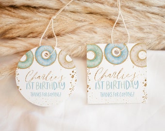 May include: Two donut-themed favor tags with gold glitter accents. The round tag says "Charlie's 1st Birthday Thanks for coming!" The square tag says "Charlie's 1st Birthday Thanks for coming!"