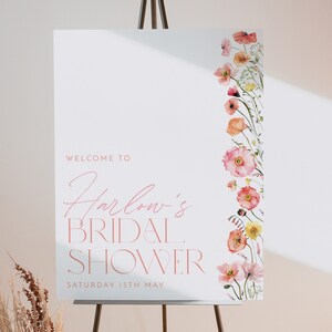 Pu&ograve; includere: Un cartello di benvenuto bianco con testo rosa che recita "Benvenuti al Bridal Shower di Harlow Sabato 15 maggio". Il cartello &egrave; decorato con una linea verticale di fiori ad acquerello rosa e arancioni.