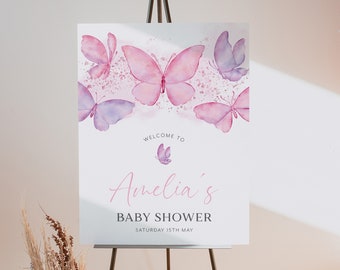 Puede incluir: Un cartel de bienvenida a la baby shower de Amelia con un diseño de mariposa acuarela rosa y morada. El cartel dice "Bienvenido a la baby shower de Amelia" y "Sábado 15 de mayo".