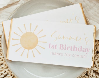 May include: White favor boxes with gold trim and a pink and gold sun design. The boxes say "Summer's 1st Birthday Thanks for Coming!"