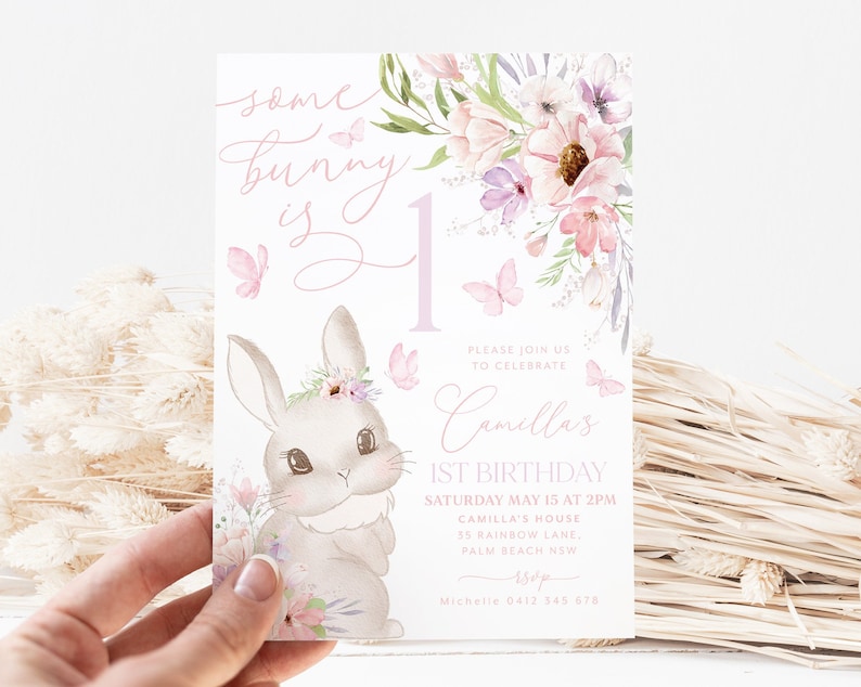 May include: A pastel-colored invitation card for a first birthday celebration. The design features a watercolor illustration of a bunny with floral accents, butterflies, and the text "Some bunny is one." The card includes event details.