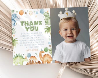 May include: A thank you card with a dinosaur theme. The card features a green and brown dinosaur, a volcano, and a green palm tree. The card also includes the text "Thank You" and "Love, George". A photo of a young child wearing a crown is in the background.