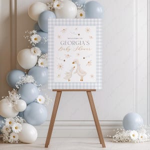 K&ouml;nnte beinhalten: Ein Willkommenszeichen f&uuml;r eine Babyparty mit einem blau-wei&szlig; karierten Hintergrund. Das Schild zeigt zwei wei&szlig;e G&auml;nse mit einem Blumenmuster und dem Text "Willkommen zur Babyparty von Georgia".