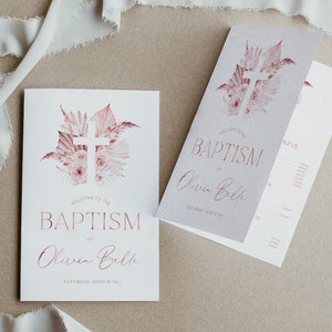 May include: Baptism invitation cards featuring a pink floral cross design. The text reads "Welcome to the Baptism of Olivia Belle, Saturday 30th June". The cards are folded and presented on a neutral surface, with a ribbon in the background.