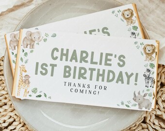 May include: Two rectangular party favors with a jungle theme. The favors are white with green text that reads "Charlie's 1st Birthday!" and "Thanks for coming!" The favors are decorated with illustrations of animals, including a lion, elephant, giraffe, zebra, and rhino.