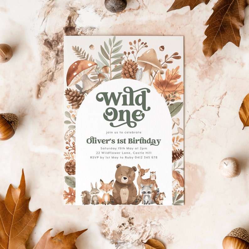 May include: A woodland-themed first birthday party invitation with a green and white archway that says "Wild One". The invitation features a brown bear, a fox, a deer, a raccoon, a hedgehog, and an owl. The text on the invitation reads "Join us to celebrate Oliver's 1st Birthday, Saturday 15th May at 2pm, 22 Wildflower Lane, Castle Hill, RSVP by 1st May to Ruby 0412 345 678".