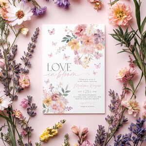 Op de afbeelding: Een bruidsdouche-uitnodiging met een bloemenmotief met vlinders en de tekst "LOVE in bloom" en "Wordt u uitgenodigd voor een bruidsdouche ter ere van Madison Hayes". De uitnodiging bevat de datum, tijd, locatie en RSVP-informatie.