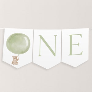 May include: A green and white banner with the word "ONE" in green letters. A small brown teddy bear is holding a green balloon on the left side of the banner.