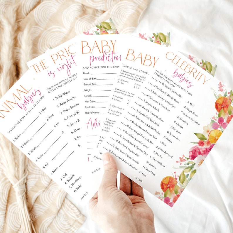 May include: A stack of baby shower game cards with floral and citrus accents. The games include "Animal Babies," "The Price is Right," "Baby Prediction," and "Celebrity Babies." The cards are held by a hand.