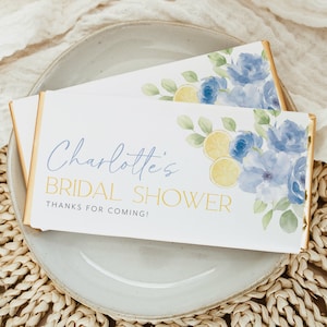 May include: A white chocolate bar favor with a blue and yellow floral design. The text on the bar reads "Charlotte's Bridal Shower Thanks for Coming!"