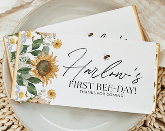 May include: A white chocolate bar with a sunflower and bee design. The text on the bar reads "Harlow's First Bee-Day! Thanks for coming!"