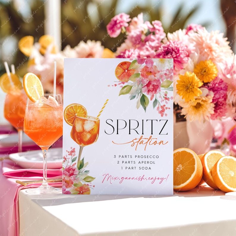 May include: A white sign with the words "Spritz Station" and a watercolor illustration of a cocktail with an orange slice. The sign also includes the recipe: 3 parts Prosecco, 2 parts Aperol, and 1 part soda. The sign is decorated with floral accents.