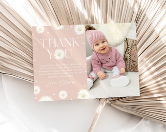 May include: A pink thank you card with a white daisy pattern and the text "THANK YOU" in a bold, modern font. The card also includes the text "Thank you so much for celebrating my 1st birthday with me and for the wonderful present you gave me! I had such a good time playing with all my friends & eating cake! Love, Olivia". A photo of a baby girl wearing a pink sweater and hat is in the bottom right corner of the card.