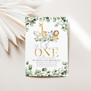 May include: A white invitation with a gold border and the text "Wild One" in gold script. The invitation features a watercolor illustration of a giraffe, elephant, lion, and zebra surrounded by eucalyptus leaves. The text "Please join us to celebrate Hudson's 1st Birthday!" is printed in black below the illustration. The date, time, and location of the party are listed below the text.