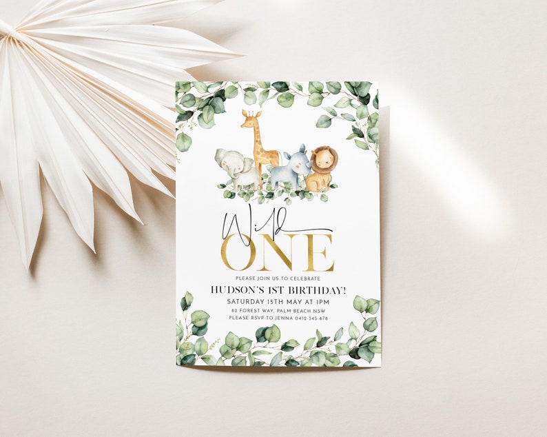 May include: A white invitation with a gold border and the text "Wild One" in gold script. The invitation features a watercolor illustration of a giraffe, elephant, lion, and zebra surrounded by eucalyptus leaves. The text "Please join us to celebrate Hudson's 1st Birthday!" is printed in black below the illustration. The date, time, and location of the party are listed below the text.
