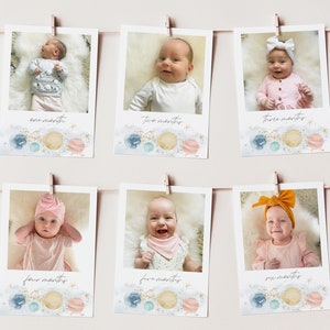 Op de afbeelding: Zes foto's van een baby in een roze en witte outfit, elke foto is gelabeld met een maand van de leeftijd van de baby. De foto's zijn in een rij gerangschikt en hangen aan een muur met wasknijpers. De foto's zijn versierd met een aquarel achtergrond van planeten en sterren.