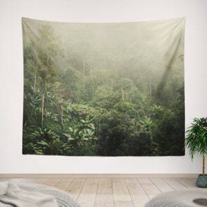 Op de afbeelding: Een wandkleed met een weelderige groene jungle scène met een mistige, etherische sfeer. Het wandkleed toont een dicht bos met hoge bomen en weelderig gebladerte, wat een gevoel van diepte en mysterie creëert.