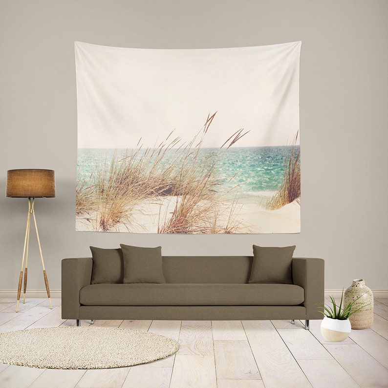 May include: A tapestry featuring a beach scene with tall grass in the foreground and a blue ocean in the background. The sky is a light blue and the sand is white.