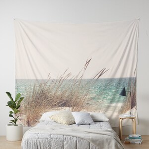 May include: A white tapestry with a beach scene featuring tall grass in the foreground and a blue ocean in the background.