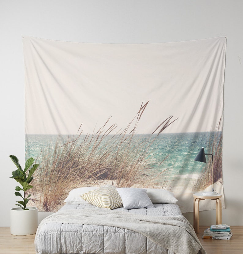May include: A white tapestry with a beach scene featuring tall grass in the foreground and a blue ocean in the background.