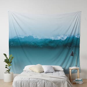 May include: A large wall tapestry featuring a photograph of a breaking ocean wave. The wave is a vibrant turquoise color, with white foam at the crest. The background fades from light blue to white.