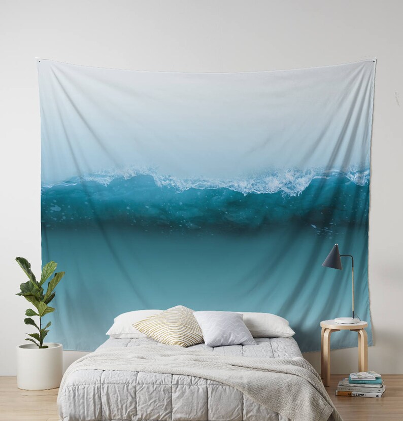 May include: A large wall tapestry featuring a photograph of a breaking ocean wave. The wave is a vibrant turquoise color, with white foam at the crest. The background fades from light blue to white.